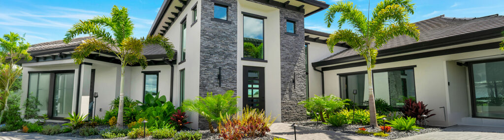 Luxury custom home exterior with stone facade, tropical landscaping, and modern design