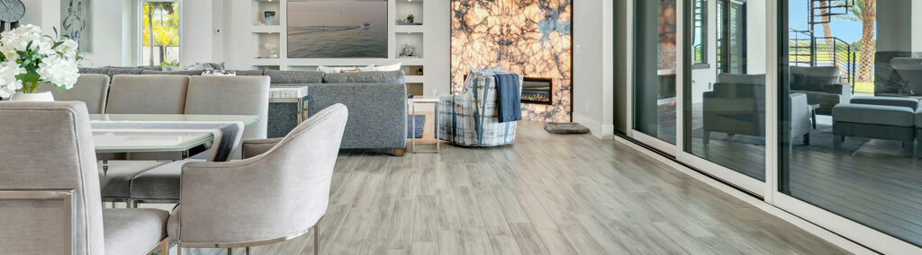 Open-concept living and dining area with light gray hardwood floors, modern furnishings, and a stone fireplace wall in a Stuart, FL home renovation.