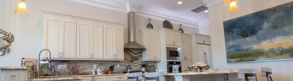 Luxury smart home kitchen renovation in Martin County featuring custom white cabinetry, marble backsplash, stainless steel appliances, and elegant coastal artwork