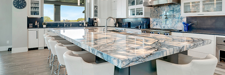 Large marble kitchen island with white and blue veining, modern white cabinetry, and matching stone backsplash