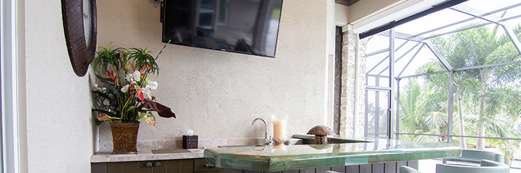 Luxury screened lanai in Martin County featuring a wall-mounted smart TV, built-in outdoor bar with stone countertops, and lush tropical