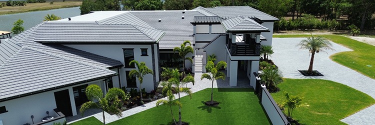 Aerial view of a completed custom home exterior in Martin County featuring white stucco finish, tile roof, lush tropical landscaping, and waterfront lot by Masterpiece Builders