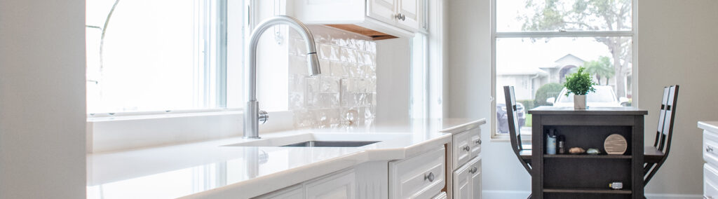 Bright white kitchen with quartz countertops, chrome pull-down faucet, and a decorative tile backsplash.