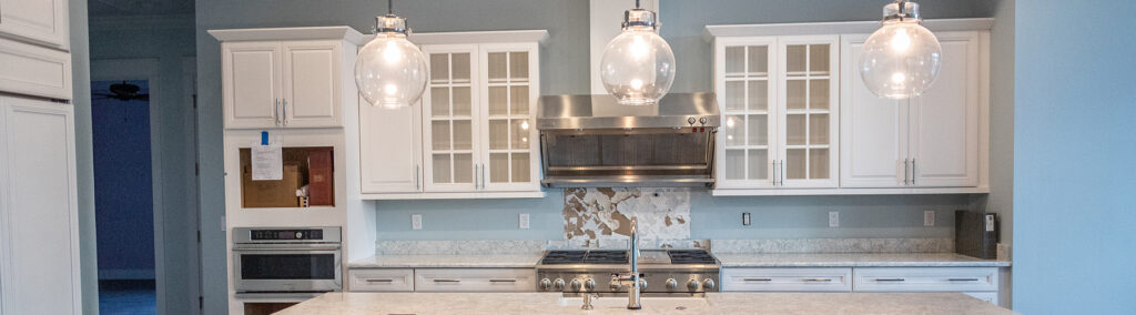 Bright, open-concept custom kitchen with white shaker cabinets, marble countertops, and globe pendant lights in a Stuart, FL home.