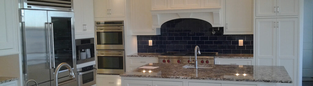 Renovated kitchen in Stuart, FL featuring white shaker cabinets, granite island countertops, stainless steel appliances, and a navy blue subway tile backsplash.