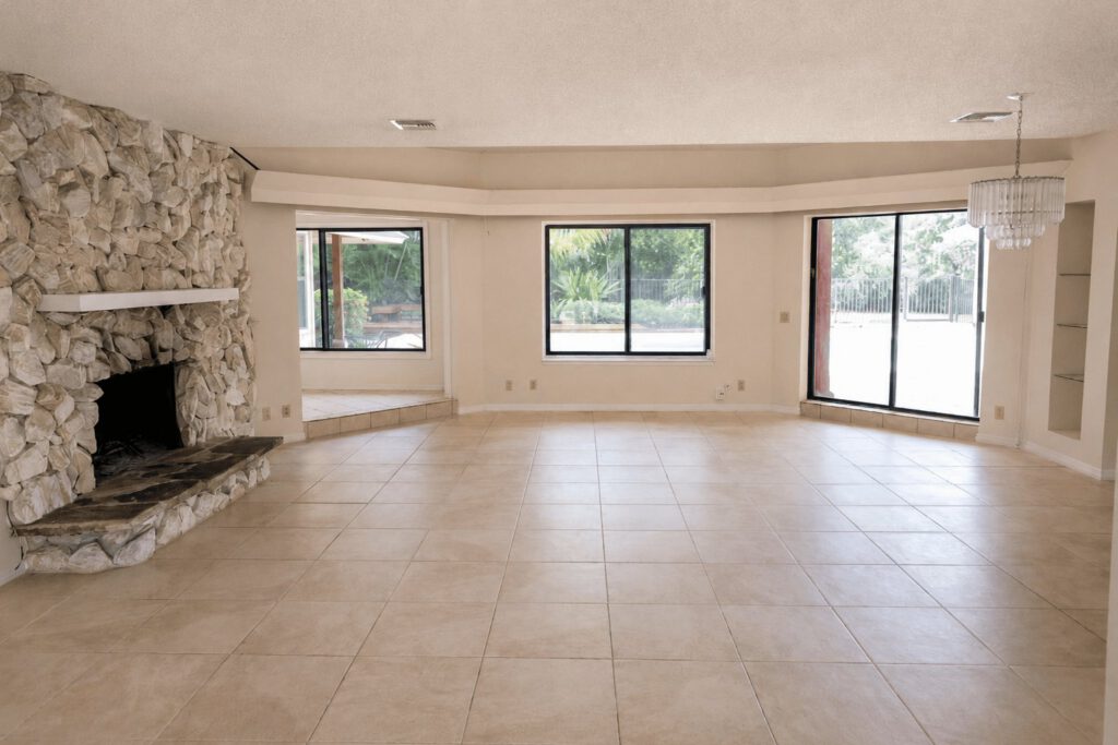 Original step-down living room with a stone fireplace and dated tile before renovation in a Snug Harbor home in Stuart, FL