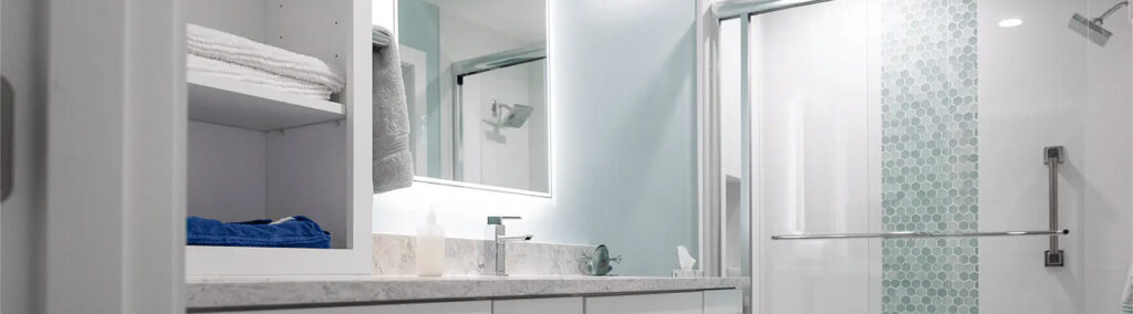 Modern ensuite bathroom with a backlit LED mirror, marble vanity, open shelving, and a glass-enclosed shower with hexagon tile accent wall.