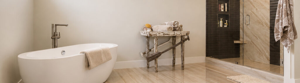 Freestanding soaking tub beside a rustic wood table, with a marble-tiled walk-in shower and warm neutral finishes.